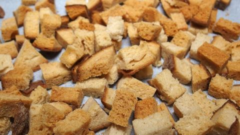 Kleine, goldbraune Croutons aus Brotresten liegen gleichmäßig auf einem Backblech in einer hellen Küche.