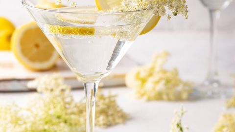 Ein elegantes Glas mit Holundersekt ohne Alkohol wird mit Zitronenscheiben und Holunderblüten dekoriert, umgeben von frischen Zitronen.