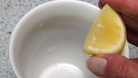 Mit Zitrone und Papierküchentüchern Teeflecken aus Porzellan und Gläsern entfernen. Ein Stück Zitrone wird über eine leere Porzellan-Tasse gehalten, um Teeflecken zu entfernen.