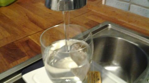 Ein Glas wird mit Wasser gefüllt, während ein Teebeutel in dem Glas liegt, um Eistee als Kaltauszug zu bereiten.