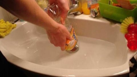 Eine Person hält eine PET-Flasche und drückt sie in ein Waschbecken mit Wasser, um eine Verstopfung zu lösen.