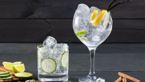 Ein eleganter Wodka-Cocktail in einem großen Glas mit Eis und Zitrusfrüchten, umgeben von Gewürzen und Limetten.
