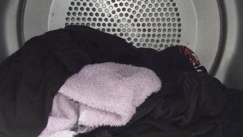 Schnellerer Trockenvorgang im Trockner - einfach ein trockenes Frotteehandtuch mit zur Wäsche geben. Im Wäschetrockner liegen Frotteehandtücher und andere Kleidungsstücke, die gerade zum Trocknen rotieren.
