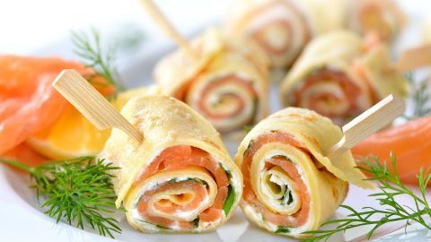 Lachsröllchen aus dünnen Omelette-Rollen mit Lachs und Kräutern werden appetitlich auf einem Teller angerichtet.