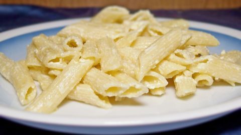 Ein Teller mit süßen Nudeln, die mit einer cremigen Frischkäse-Sauce überzogen sind, auf einem blauen Tuch serviert.