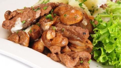 Saftiges Boeuf Stroganoff liegt auf einem Teller, umgeben von Püree und frischem Salat, garnierter mit Petersilie.