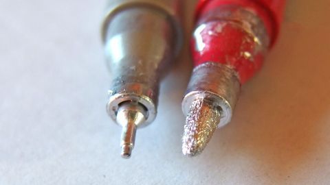 Ein Lackmalstift liegt nebeneinander mit einem eingetrockneten Ende, während das andere eine beschädigte Spitze zeigt.