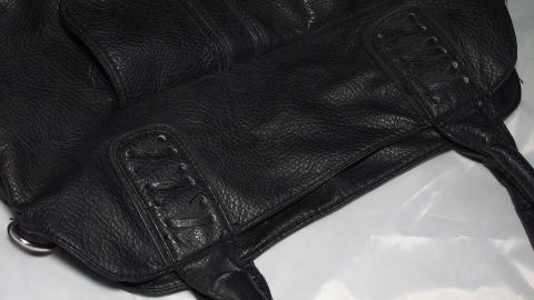 Eine schwarze Ledertasche liegt auf einer hellen Oberfläche, während sie mit Melkfett gepflegt wird, um die Haut zu schützen.