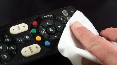 Schmutzige und verklebte Fernbedienung ganz einfach und schnell reinigen. Eine Hand reinigt mit einem Tuch eine schmutzige Fernbedienung, um sie wieder sauber zu machen.