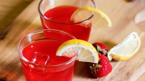 Zwei Gläser mit Erdbeerlimes stehen auf einem Holzbrett, dekoriert mit Zitronenscheiben und frischen Erdbeeren.