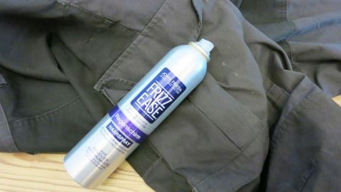 Ein Spray für frische Farbe liegt auf einer dunklen Stoffoberfläche, um Kleidung von angetrockneter Farbe zu befreien.