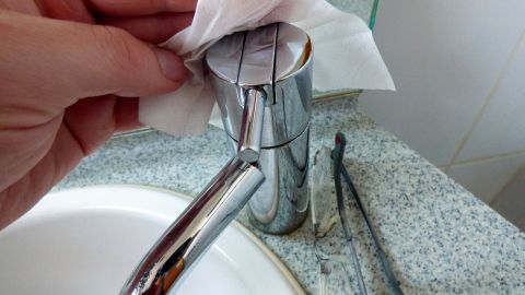 Ein Brillenputztuch wird benutzt, um die gl&auml;nzende Oberfl&auml;che einer Badarmatur zu reinigen, w&auml;hrend es in einem Badezimmer ist.