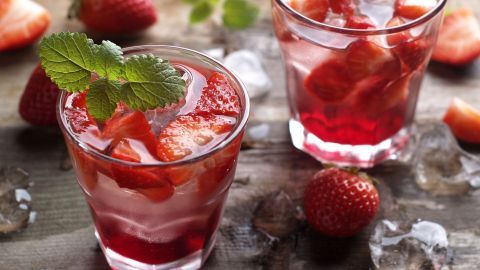 Zwei Gläser Kirsch-Erdbeer-Bowle mit frischen Erdbeeren und Minze stehen auf einer rustikalen Holzplatte, umgeben von Eis.