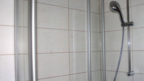 Babyöl ist ein echtes Multitalent: Nach dem Putzen kann man es einfach auf die Fliesen in der Duschkabine auftragen. Kalk kann sich schwerer ablagern und es riecht auch noch ganz lecker. Eine Duschkabine mit glatten Wänden und einem Duschkopf, die bereit ist, um Kalkablagerungen zu reduzieren, steht im Badezimmer.