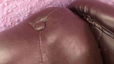 Ein Kunstledersofa mit sichtbaren Verfärbungen und Flecken im Nahbereich, an einer pinken Wand.