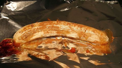 Eine gegrillte Banane liegt auf Aluminiumfolie, überzogen mit Honig und Schokolade, bereit für den Genuss im Freien.