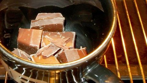 Im schwarzen Becher schmelzen Stücke von Blockschokolade auf einem Gitterrost, um leckere Kuvertüre zuzubereiten.