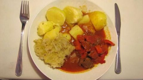 Ein schmackhaftes Gulasch ähnlicher ungarischer Art auf einem Teller, umgeben von kartoffeln und Reis, serviert auf einem Tisch.
