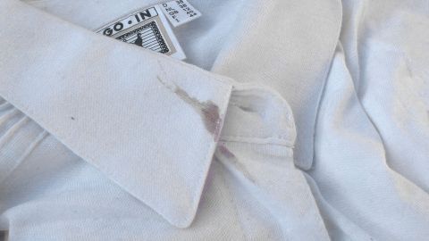 Mit dieser selbst gemachten Gallseifen-Waschpulver-Mischung kann man die unterschiedlichsten Flecken sehr gut entfernen. Ein weißes Hemd mit einem sichtbaren Fleck am Kragen liegt auf einer Oberfläche, während die Gallseife zur Fleckentfernung bereitsteht.