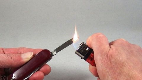 Ein Taschenmesser mit einer angezündeten Flamme wird mit einem Feuerzeug entzündet, um es möglicherweise zu desinfizieren.