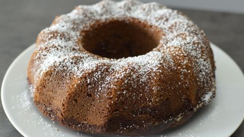 Ein Gugelhupf, aus Marmor mit Eierlikör, steht auf einem weißen Teller und ist mit Puderzucker bestäubt.
