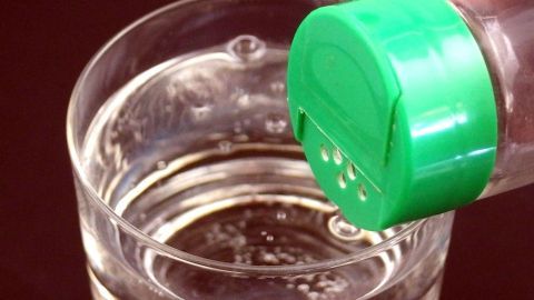 Mit ein paar - wenigen - Körnchen Salz geht die Kohlensäure raus, ohne dass das Wasser salzig schmeckt. Ein grüner Verschluss einer Kohlensäureflasche wird über ein Glas mit sprudelndem Mineralwasser gehalten, bereit zum Einschenken.