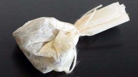 Gewürze wie Lorbeerblätter oder Nelken zum Mitkochen in Speisen, in einen Teebeutel geben. Ein Teebeutel aus durchsichtigem Stoff liegt auf einer dunklen Oberfläche, bereit für Gewürze beim Kochen.