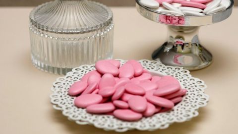 Eine silberne Schale und ein Glasbehälter mit rosa Süßigkeiten stehen auf einem eleganten Tablett in sanfter Beleuchtung.
