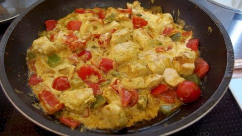 In einer Pfanne brät ein buntes Curry-Gemüse-Geschnetzeltes, das mit roten Tomaten und grünen Paprika reichhaltig befüllt ist.