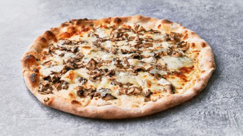 Eine frisch gebackene Pizza liegt auf einem grauen Untergrund und zeigt eine goldene Kruste mit Pilzen und Käse.