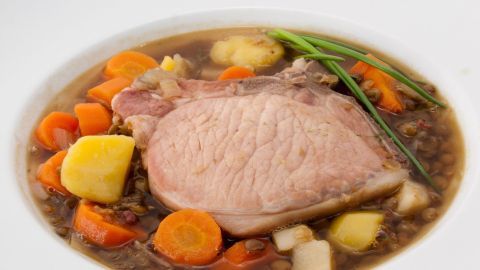 Ein großer Teller zeigt Rübenmus mit Kasseler und Kochwurst, umgeben von buntem Gemüse in einer klaren Brühe.