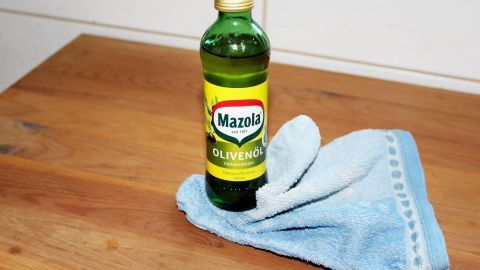 Ein Flasche Olivenöl steht auf einem Holzoberfläche, umgeben von einem blauen Tuch, bereit zur Behandlung von Kiefernmöbeln.