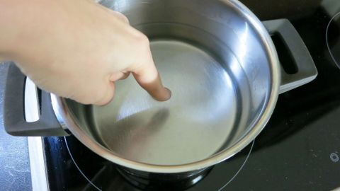 Ein Tipp zum Schmunzeln: Zeigefinger etwa 5 Sekunden in das Wasser halten. Wenn sich die Haut leicht abschält, ist das Wasser gar. Ein Finger zeigt auf Wasser in einem Topf auf einem Herd, während das Wasser erhitzt wird. Wann ist Wasser gar?