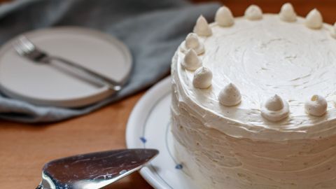 Eine Buttercremetorte steht auf einem Teller, während ein Tortenschneider bereit ist, sie zu servieren.