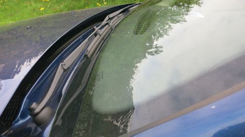 Eine beschlagene Autoscheibe zeigt, wie sich Feuchtigkeit auf dem Glas im Freien sammelt, umgeben von grüner Natur.