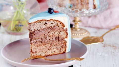 Eine frische, mehrschichtige Buttercremetorte steht auf einem Teller, während eine Glasglocke sie schützt.
