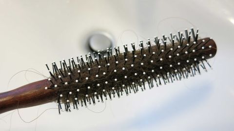 Eine Rundbürste mit Haaren hängt über einem Waschbecken, wo sich ein Abfluss befindet. Haare in Abfluss entfernen.