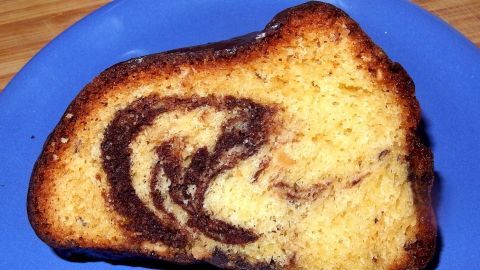 Ein Marmorkuchenstück liegt auf einem blauen Teller. Die Schichten aus hellem und dunklem Teig sind deutlich sichtbar.