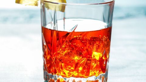 Ein Glas Spritz steht auf einem Tisch, gefüllt mit leuchtend rotem Getränk und einem Zitronenschnitz am Rand.