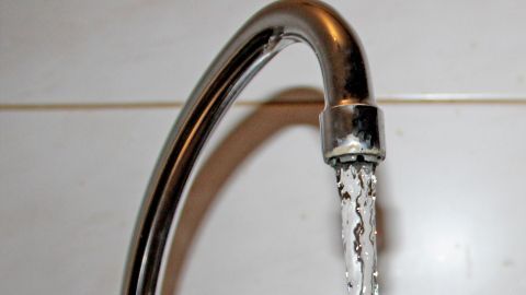 Ein Wasserhahn sprudelt frisches Leitungswasser, das in einem modernen Badezimmer aus glänzenden Fliesen fließt.