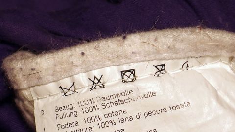 Pflegehinweise auf einem Textiletikett zeigen Waschsymbole und Materialzusammensetzung für die Reinigung von Kleidung.