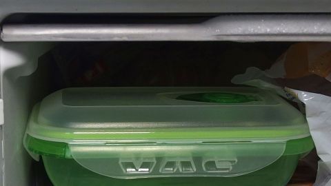 Eine grüne Tupperdose steht im Kühlschrank und könnte Gerüche aufnehmen, während sie auf einem Regal verstaut ist.