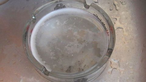 Verschmutzte Aschenbecher ganz einfach reinigen mit heißem Wasser und Waschpulver. Ein Aschenbecher liegt im Wasser eines Spülbeckens und wird gerade gereinigt, um wieder sauber wie neu zu sein.
