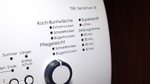Ein Trockner mit verschiedenen Programmen und einem Knopf zur Einstellung für die Pflegeleicht-Funktion steht an einer Wand.