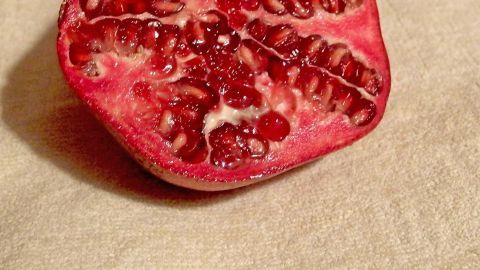Ein aufgeschnittener Granatapfel liegt auf einem hellen Hintergrund, bereit, um seine Spritzer zu zeigen.