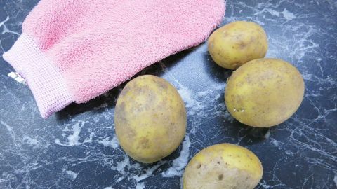 Mit einem Peelinghandschuh aus dem Drogeriemarkt kann man ganz hervorragend Kartoffeln unter Wasser abreiben. Kartoffeln liegen auf einer dunklen, marmorierten Oberfläche, während ein pinker Peelinghandschuh daneben liegt.