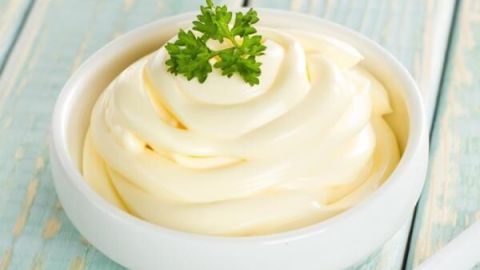 Eine Schale Mayonnaise ruht mit Petersilienblatt auf rustikalem, hellblauem Holztisch.
