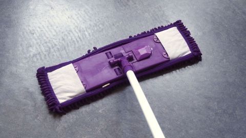 Ein lila Wischmopp liegt auf einem glatten, dunklen PVC-Bodenbelag und wird zur Reinigung verwendet.
