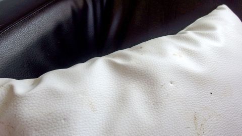 Ein Kissen liegt auf einem dunklen Sofa, die Oberfläche ist zerknittert und hat kleine Flecken, was seine Praktikabilität beeinträchtigt.