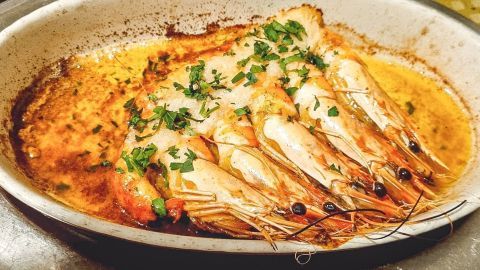 Garnelen sind in einer Auflaufform mit Kokosmilch und frischem Grün garniert, umgeben von einer goldenen Sauce.
